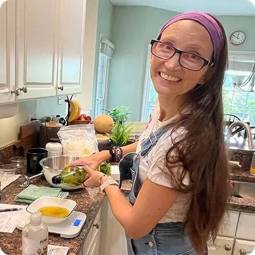 Allison Savino smiling as she pours oil into a mixing bowl while making soap in her kitchen.