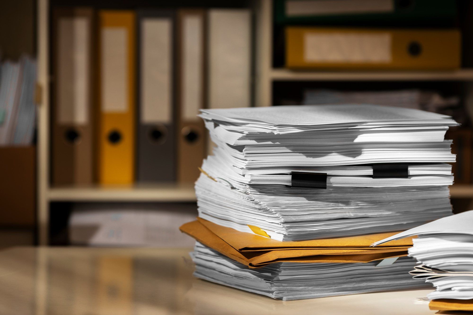 A tall stack of paper records and folders on a desk.